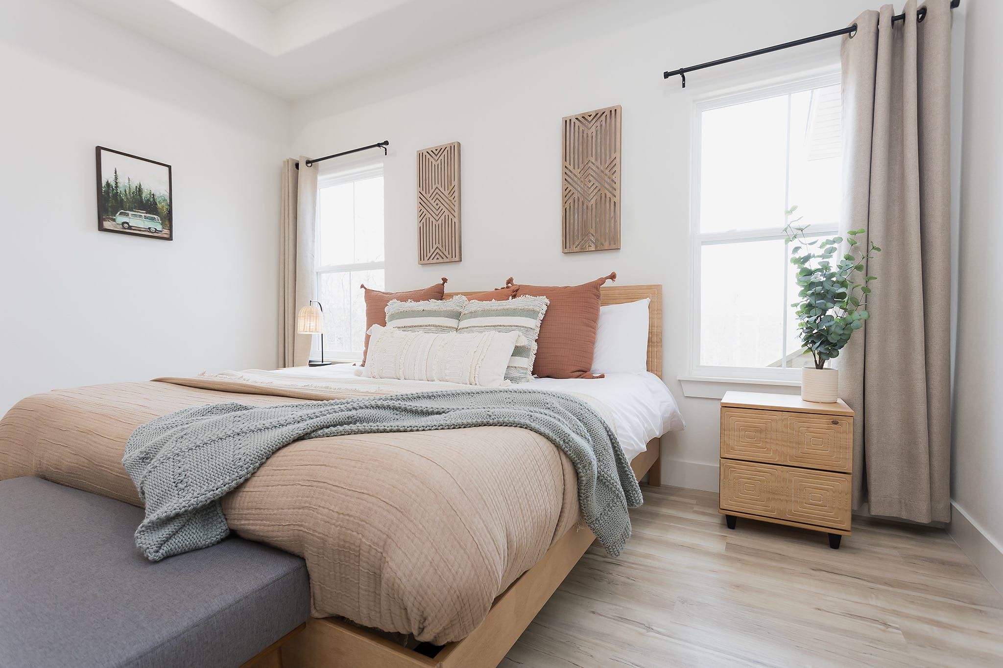 Un dormitorio con cama, mesitas de noche, una ventana y una planta.