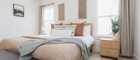 Un dormitorio con cama, mesitas de noche, una ventana y una planta.