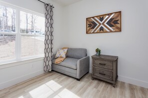 Huoneessa on harmaa sohva, puinen kaappi, kuviollinen verho ja geometrisesti kuvioitu seinätaideteos.
