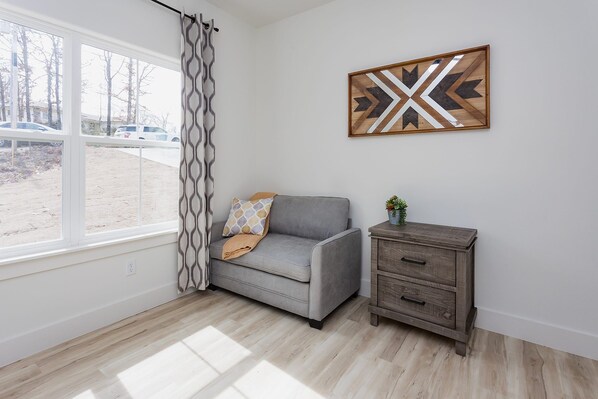 A room with a grey sofa, a wooden cabinet, a patterned curtain, and a geometric wall art piece. - Ridgeline Retreat, Your Gateway to NWA Adventure! (Bella Vista)