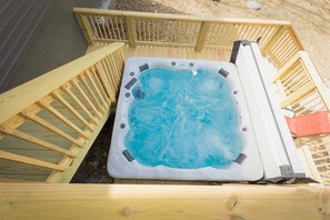 A hot tub with a wooden deck and railings, surrounded by a sandy area. - Ridgeline Retreat, Your Gateway to NWA Adventure! (Bella Vista)