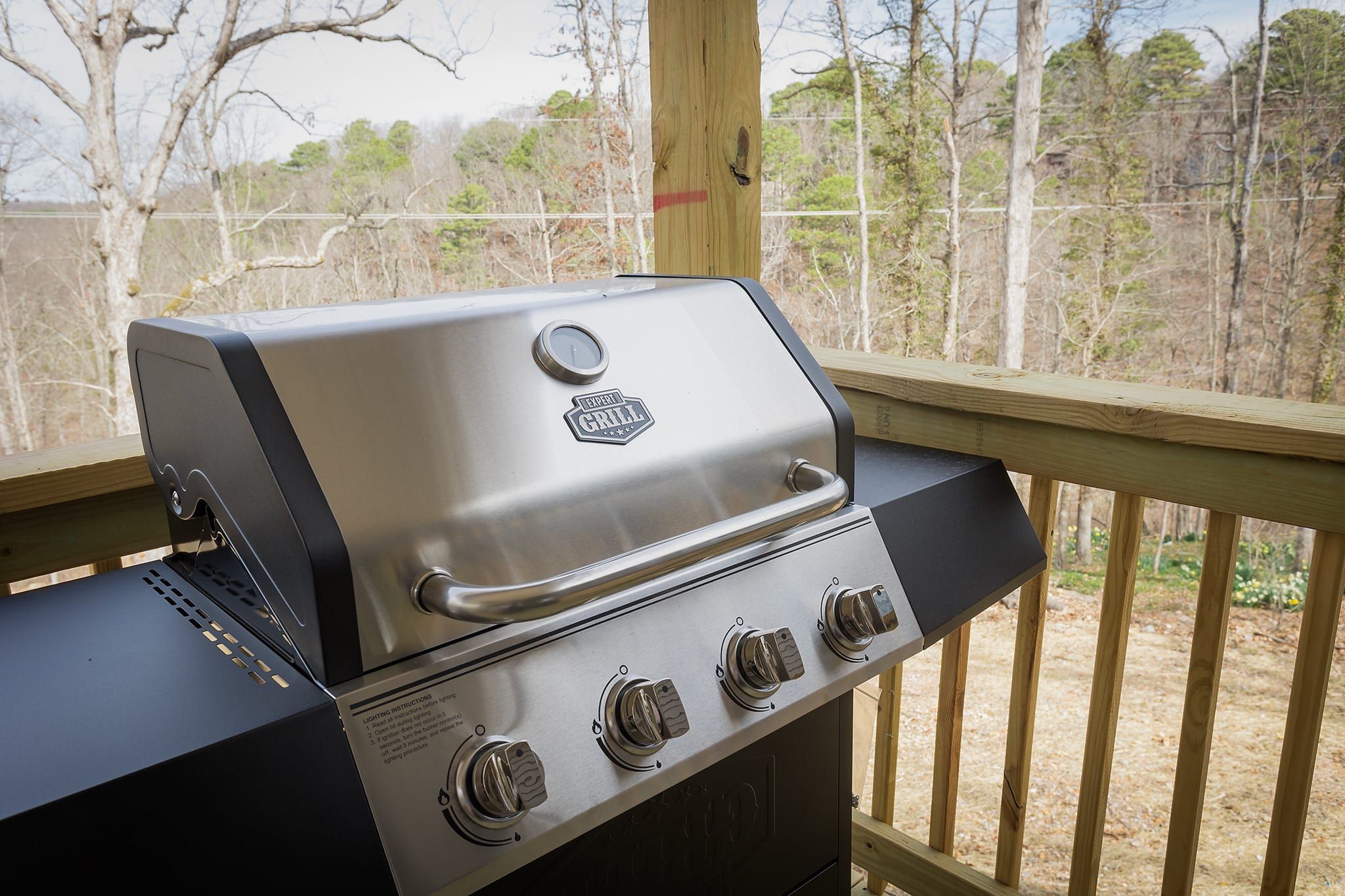 A stainless steel grill with four knobs, a digital display, and a logo on the lid, placed on a wooden deck.
