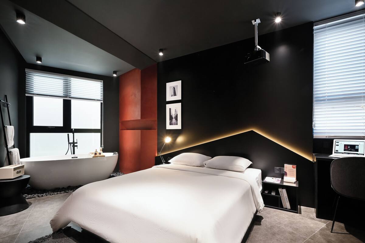 A modern bedroom with a large bed, a bathtub, and a desk with a laptop.