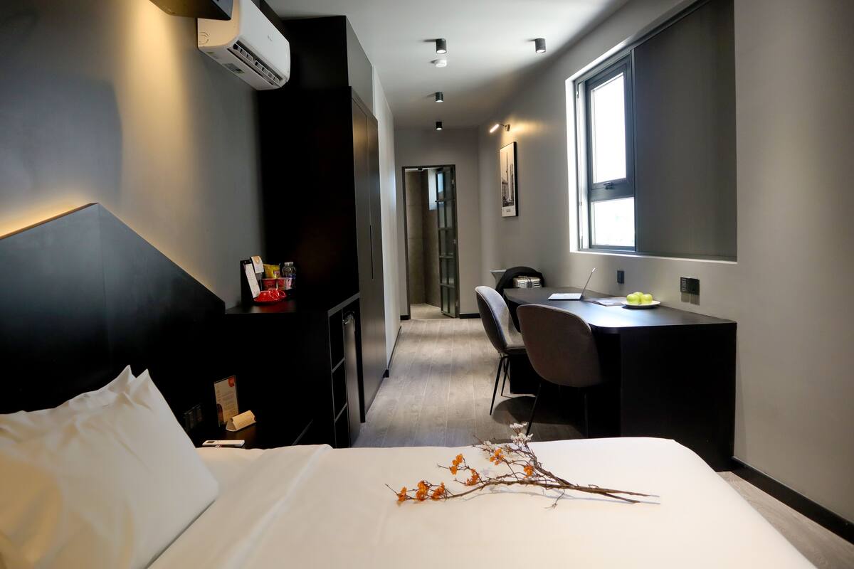 A modern hotel room with a bed, a desk, a chair, and a large window.