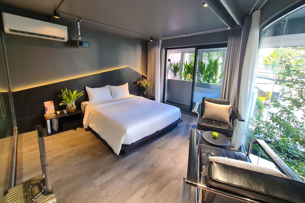 A modern hotel room with a large bed, a small balcony, and a seating area with a table and chairs.