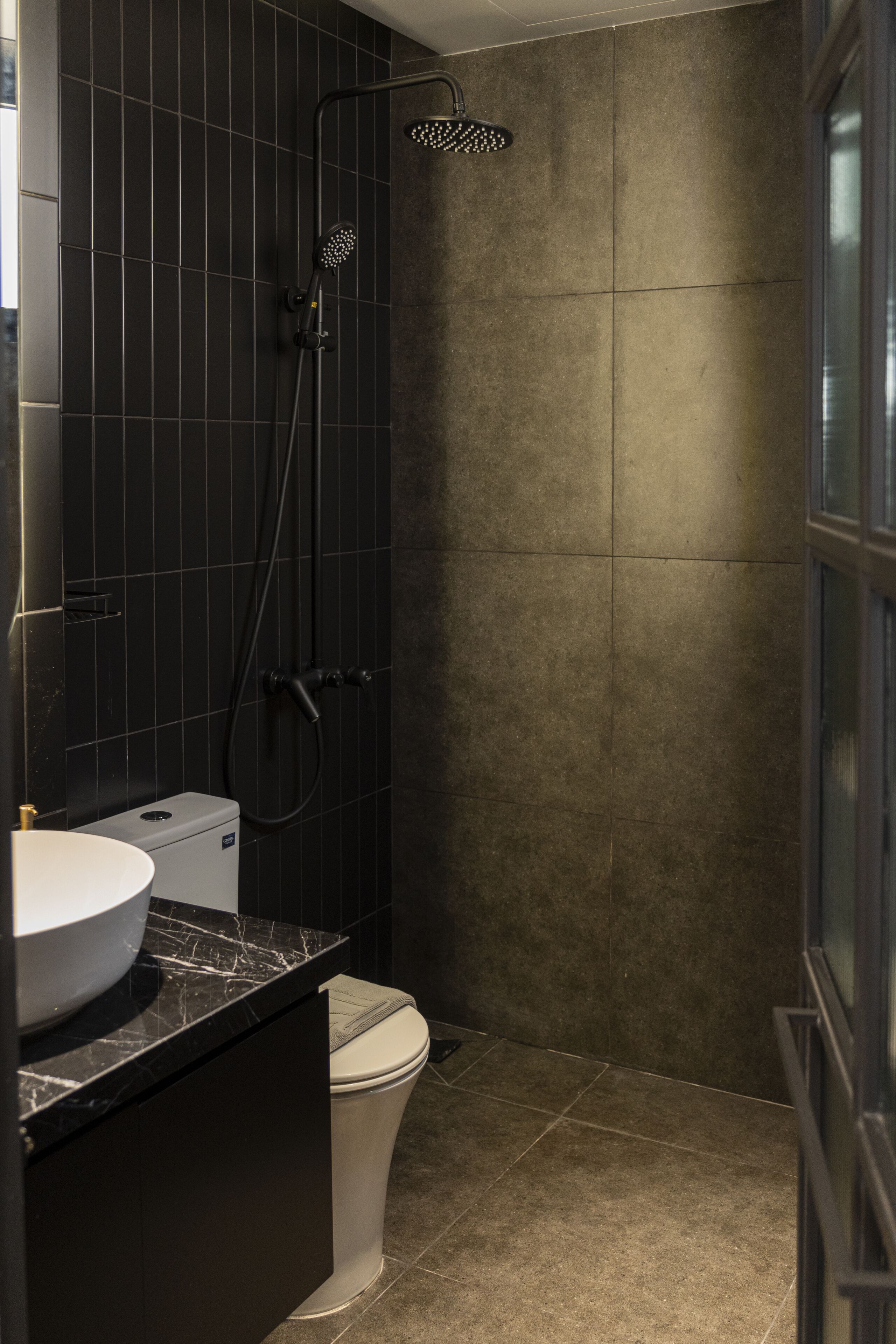 A modern bathroom with a black tiled shower, a white toilet, and a marble countertop.