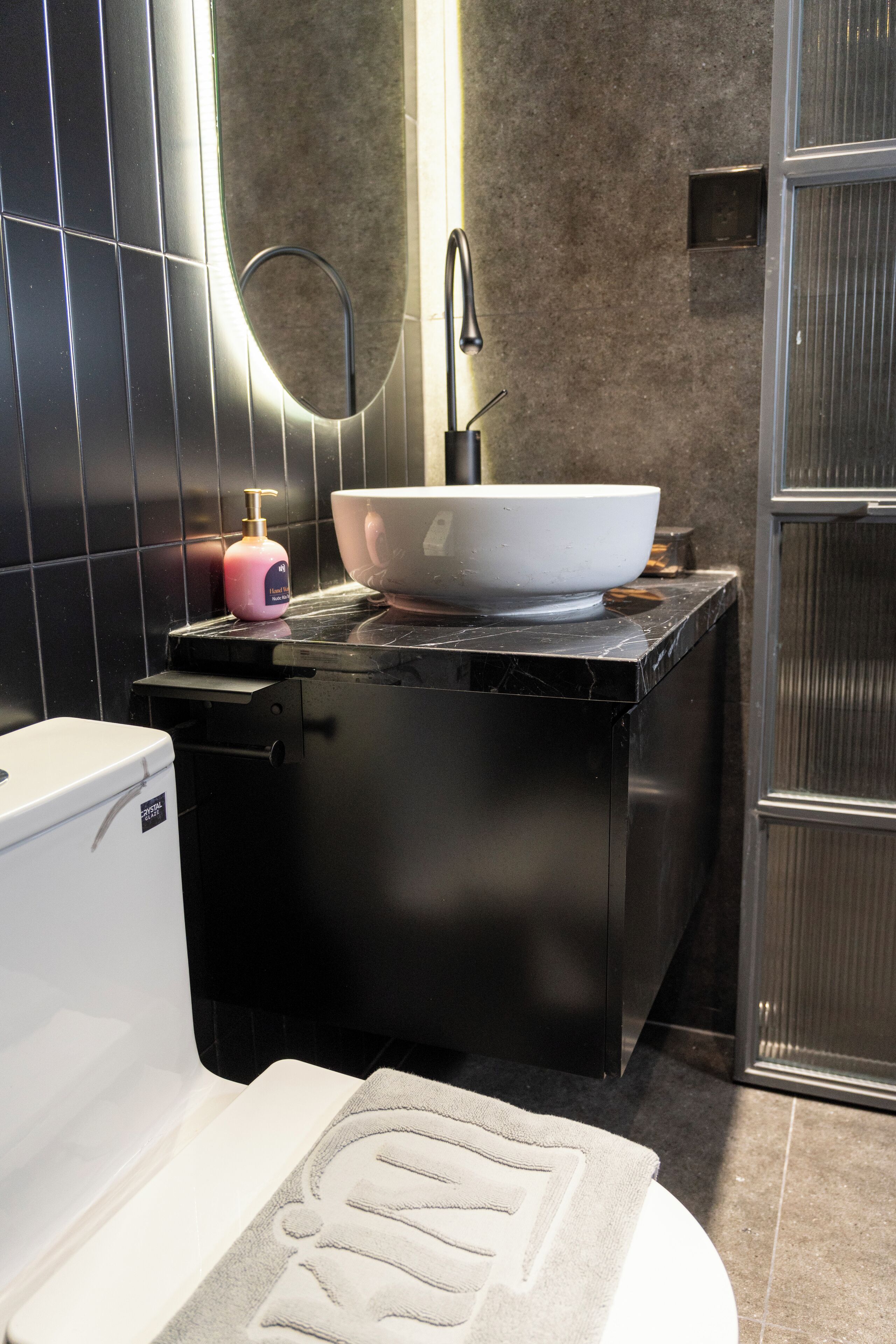 A bathroom with a white toilet, a sink with a large basin, a mirror, and a soap dispenser.