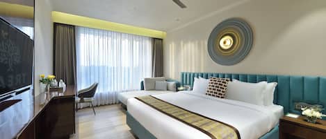 A hotel room with a large bed, a desk, a chair, a TV, and a ceiling fan.