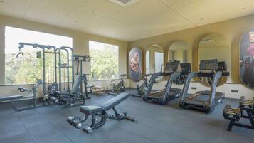 A gym with various exercise equipment, large windows, and mirrors on the walls.