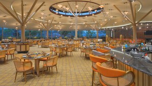 A spacious indoor dining area with multiple tables and chairs, a central bar, and a high ceiling with hanging lights. - URBANE BY TREAT  (Daman)