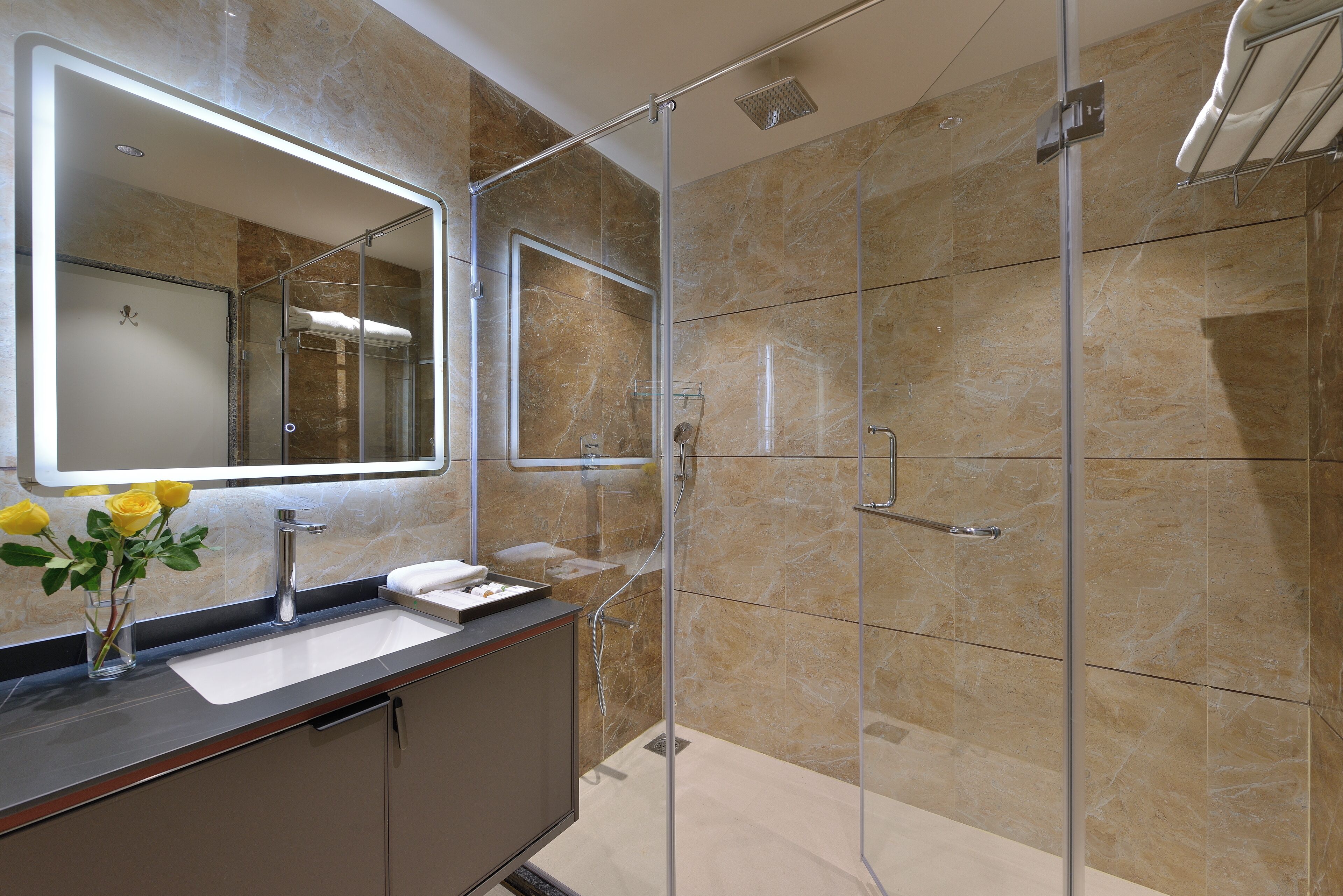 A modern bathroom with a glass-enclosed shower, a vanity with a mirror, and a vase with yellow flowers.
