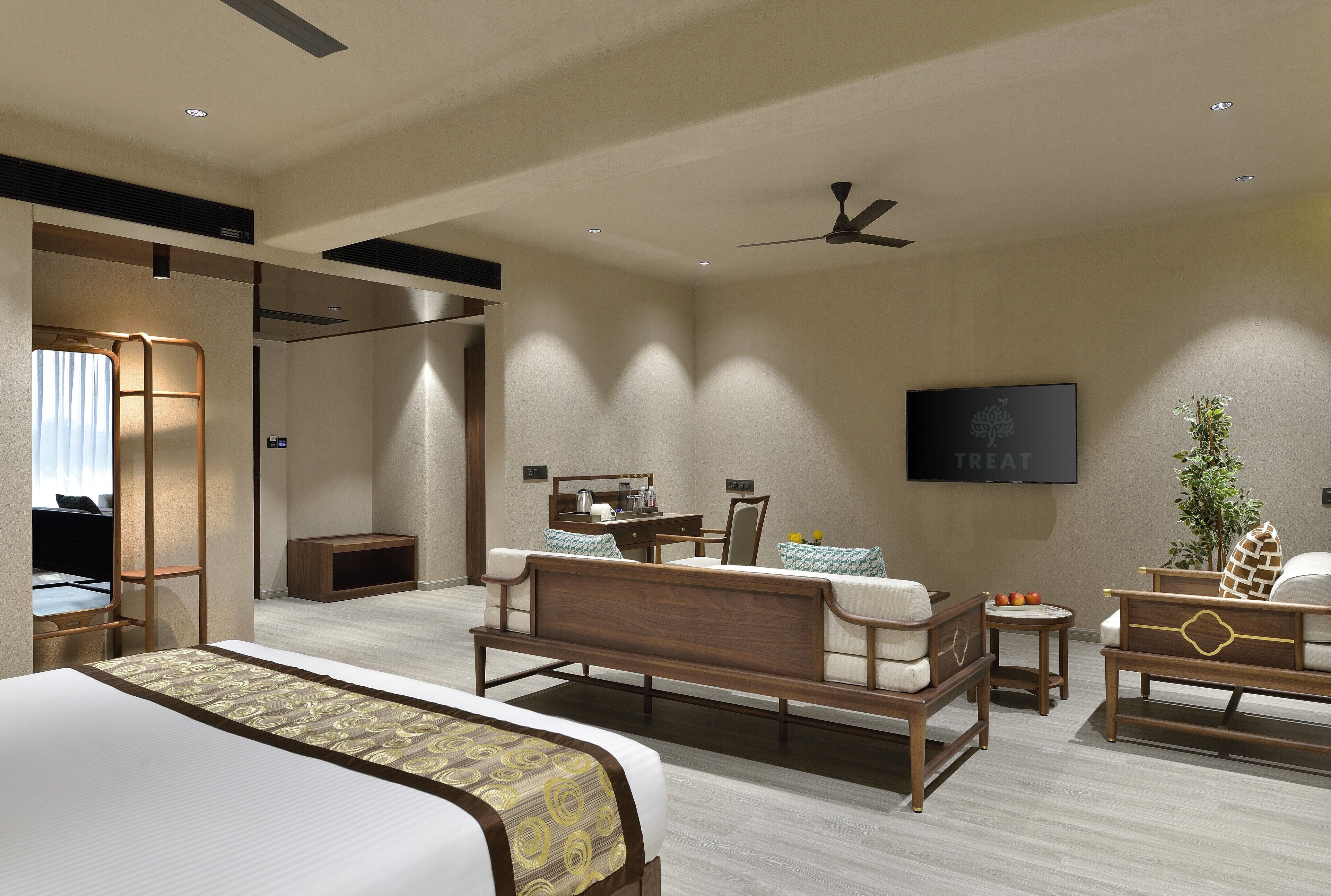 Ein modernes Hotelzimmer mit einem großen Bett, einem Schreibtisch, einem Sessel, einem Fernseher und einem Deckenventilator.