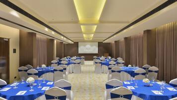Un salón de conferencias con filas de mesas, cada una cubierta con un mantel azul y sillas blancas.