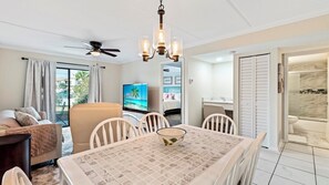 A modern living room with a dining table, chairs, a sofa, a TV, and a ceiling fan.