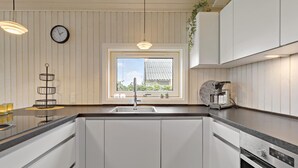 A modern kitchen with white cabinetry, a built-in oven, a coffee maker, and a window with a view of a house. - 2 bedroom nice home in Kerteminde (Kerteminde)