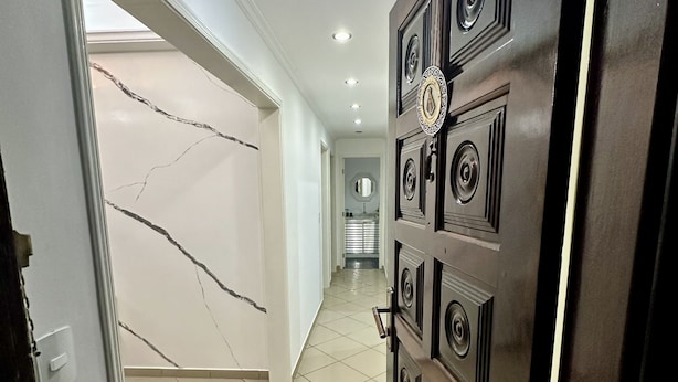 A hallway with a tiled floor, a door with a decorative panel, and a ceiling with recessed lighting. - Apartamento a 4 min da Basílica  (Aparecida)