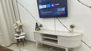 A modern living room with a flat-screen TV mounted on the wall, a white entertainment unit below, and a brown sofa. - Apartamento a 4 min da Basílica  (Aparecida)