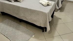 A hotel room with two beds, beige bedding, a patterned rug, and a window with curtains. - Apartamento a 4 min da Basílica  (Aparecida)