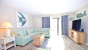 A living room with a light blue sofa, a wooden coffee table, a white side table, a blue rug, a wooden cabinet, and a television on a stand. - Wight Bay 223-Baywater 47th St, Pool, Elev, W/D, AC, Free WIFI (Ocean City)