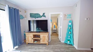 A living room with a wooden entertainment unit, a flat-screen TV, and a teal decorative shelf. - Wight Bay 223-Baywater 47th St, Pool, Elev, W/D, AC, Free WIFI (Ocean City)