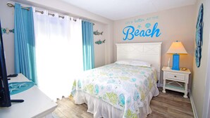 A bedroom with a bed, curtains, a nightstand, a lamp, and a wall decoration. - Wight Bay 223-Baywater 47th St, Pool, Elev, W/D, AC, Free WIFI (Ocean City)
