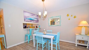 A dining area with a white table and turquoise chairs, a painting on the wall, and a mirror with a decorative frame. - Wight Bay 223-Baywater 47th St, Pool, Elev, W/D, AC, Free WIFI (Ocean City)