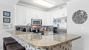 A modern kitchen with white cabinets, a granite island, stainless steel appliances, and a decorative metal wall piece. - PI 607: The Nautical Nook - Your Perfect Beachside Escape! (Fort Walton Beach)