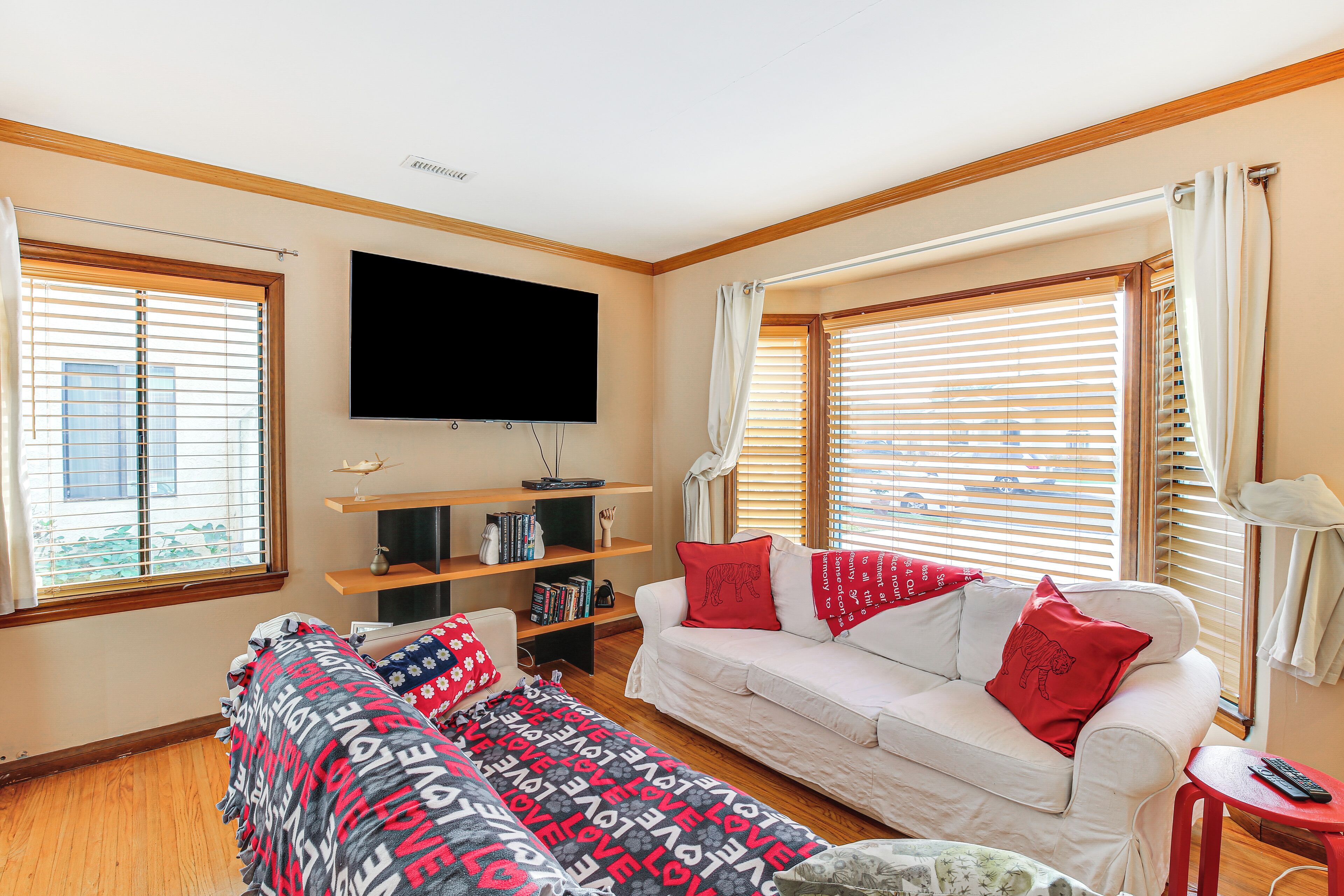 A living room with a white sofa, a flat-screen TV mounted on the wall, and a bookshelf with books and decorative items.