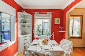 Uma área de refeições com uma mesa posta para quatro pessoas, uma cadeira branca com almofada listrada e um aparador branco com prateleiras.