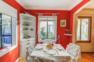 Un comedor con una mesa preparada para cuatro personas, una silla blanca con cojín a rayas y un aparador blanco con estantes.