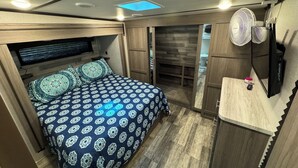 Ein kleines Schlafzimmer mit Bett, Fernseher, Deckenventilator und Holzschrank.