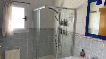 Un baño con ducha envuelta en vidrio, un lavabo blanco y un espejo con marco azul.