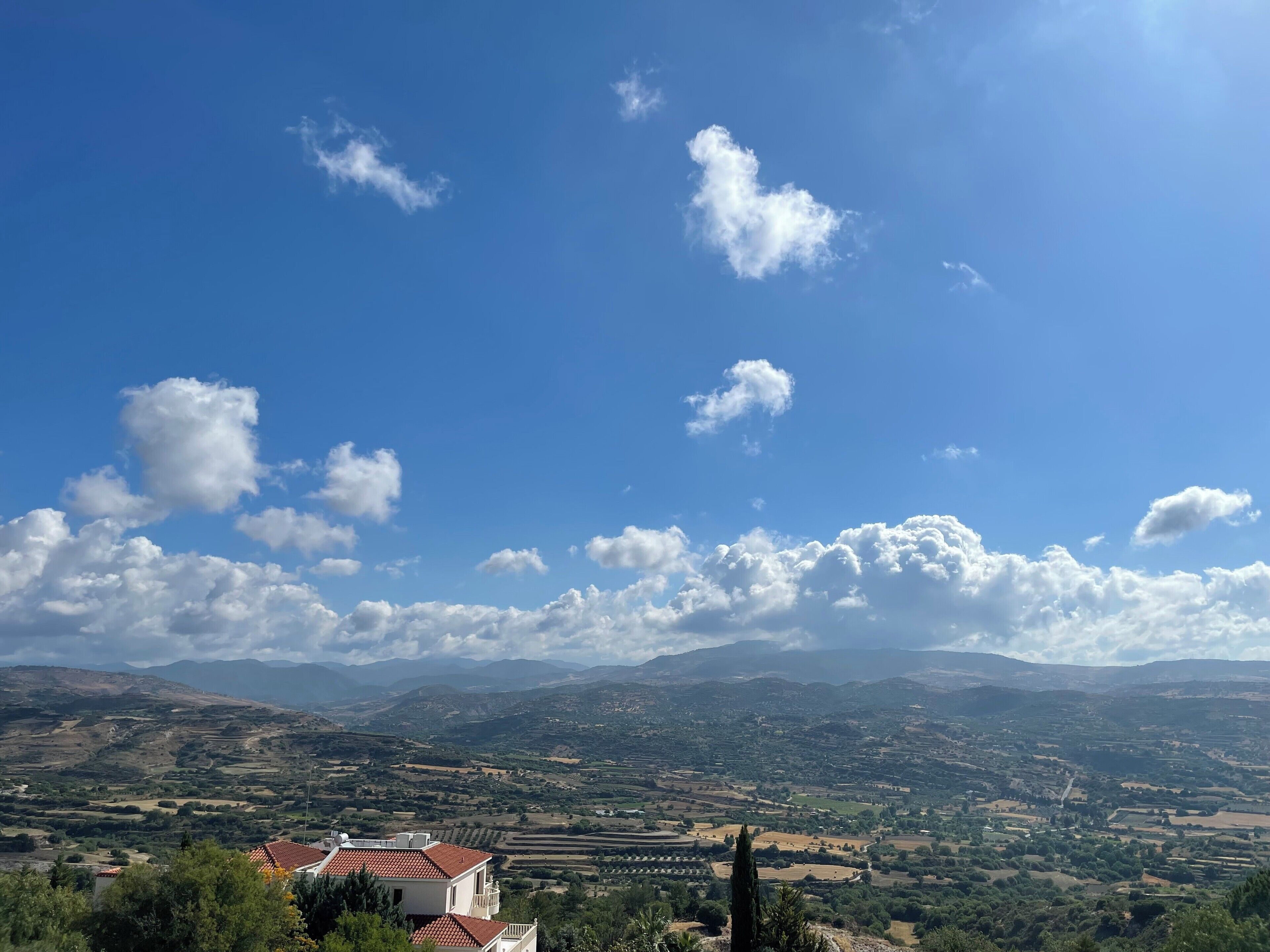 A panoramic view of a rural landscape with rolling hills, a clear blue sky, and scattered clouds.