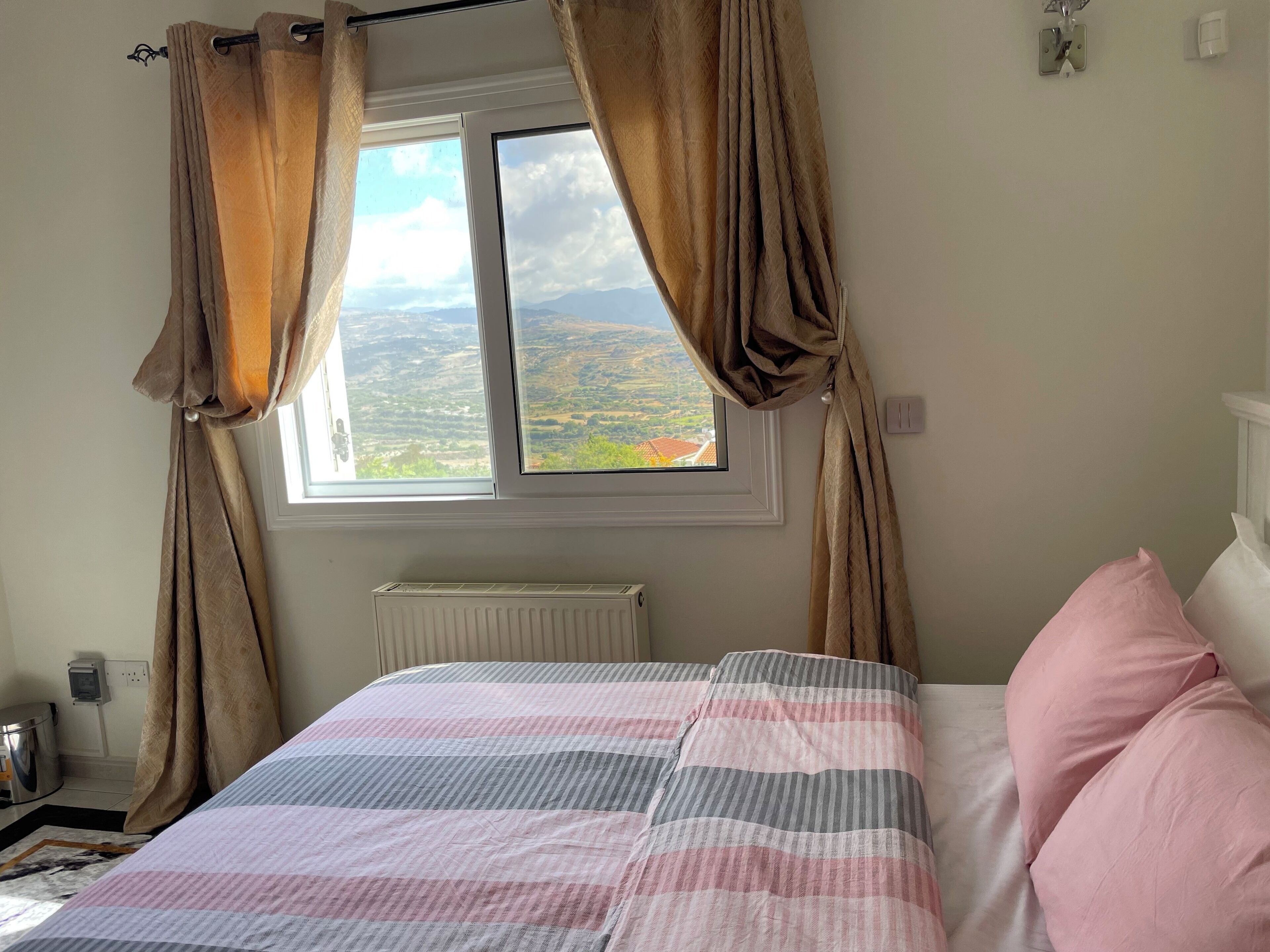 A bedroom with a bed, curtains, a radiator, and a window with a view of the countryside.