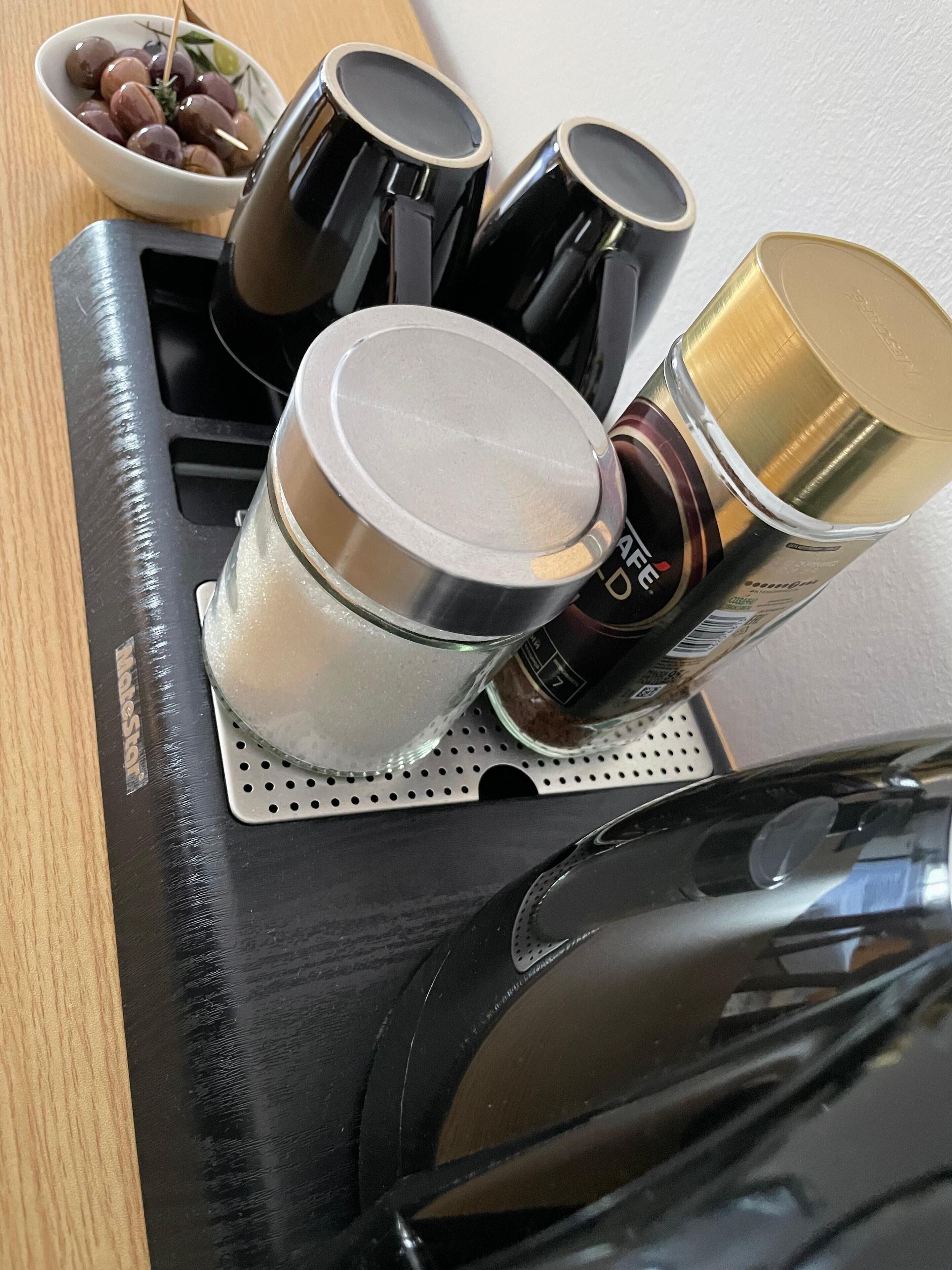 A kitchen counter with a coffee maker, a kettle, a jar of sugar, and a bowl of grapes.