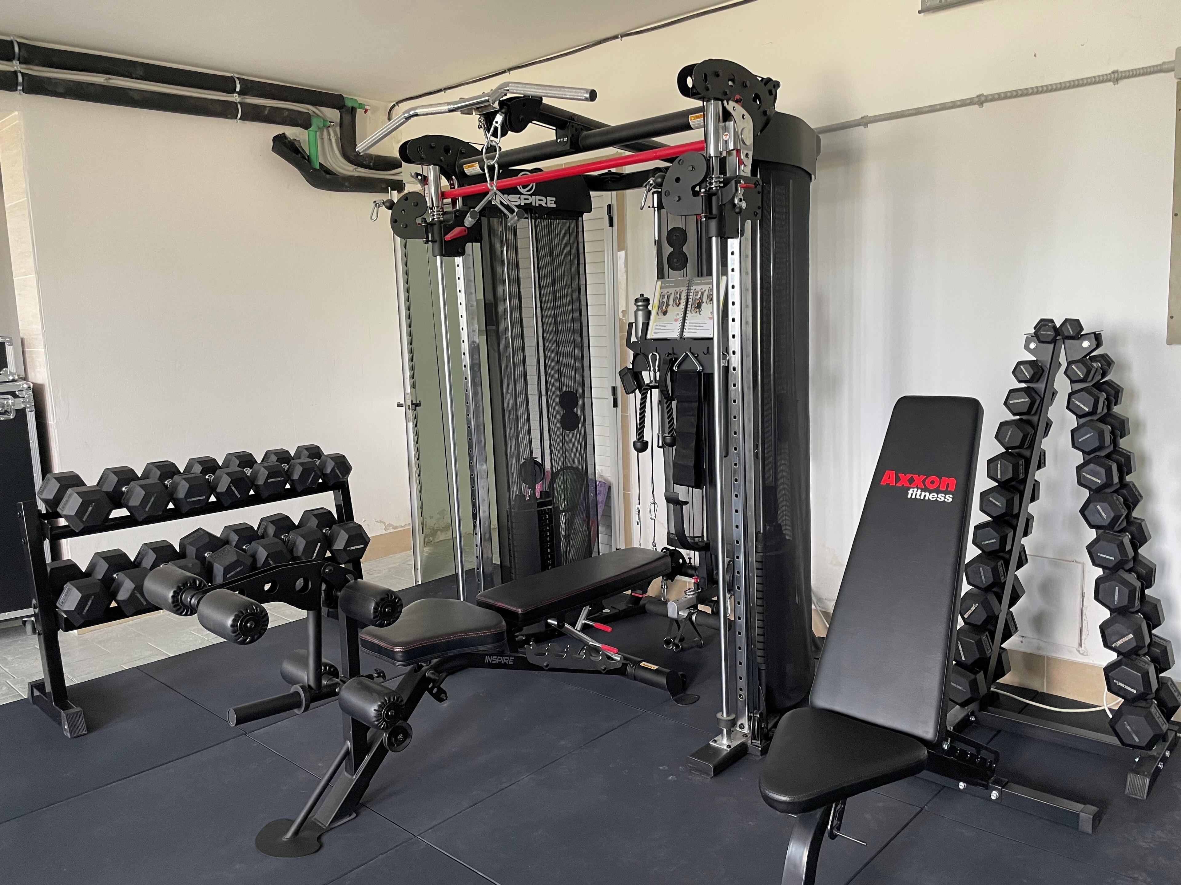 Een sportschool met een bankdrukrek, gewichten en een kabelapparaat.