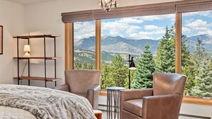 A bedroom with a large window, a bed, two chairs, a small table, and a lamp. - Aspen Spirit Vacation Home At Windcliff 3 Bedroom Home by RedAwning (Estes Park)