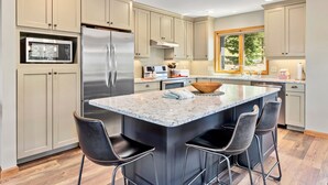 A modern kitchen with beige cabinetry, a stainless steel refrigerator, a microwave, and a large island with bar stools. - Aspen Spirit Vacation Home At Windcliff 3 Bedroom Home by RedAwning (Estes Park)