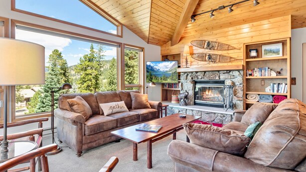 A cozy living room with a stone fireplace, leather sofas, and a large window offering a scenic view. - Aspen Spirit Vacation Home At Windcliff 3 Bedroom Home by RedAwning (Estes Park)