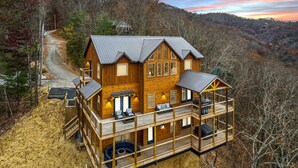 A multi-story log cabin with a balcony, surrounded by a forested landscape. - Treehouse Lodge 5 Bedroom Cabin by RedAwning (Sevierville)