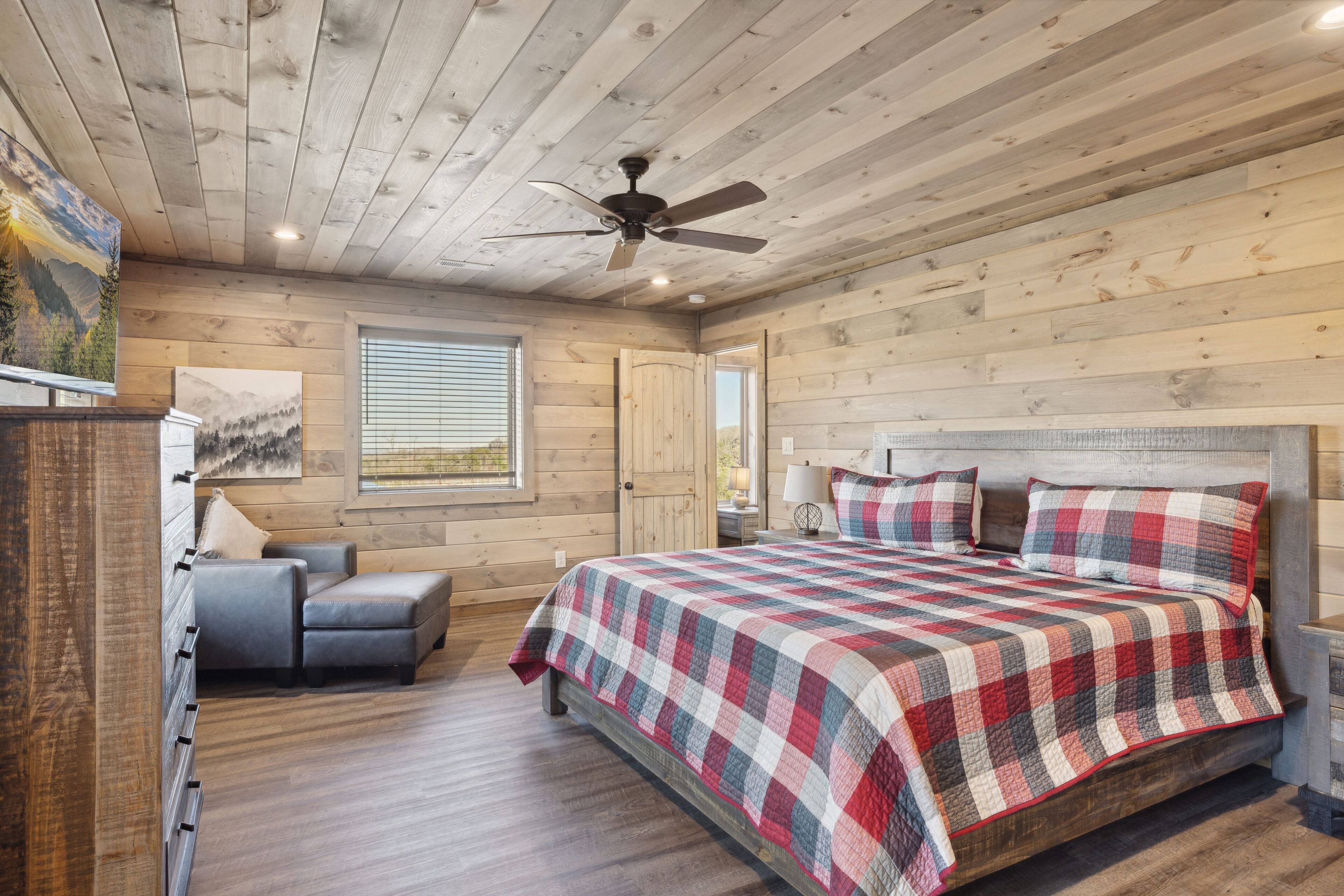 A log cabin bedroom with a bed, a gray sofa, a ceiling fan, and wooden walls.