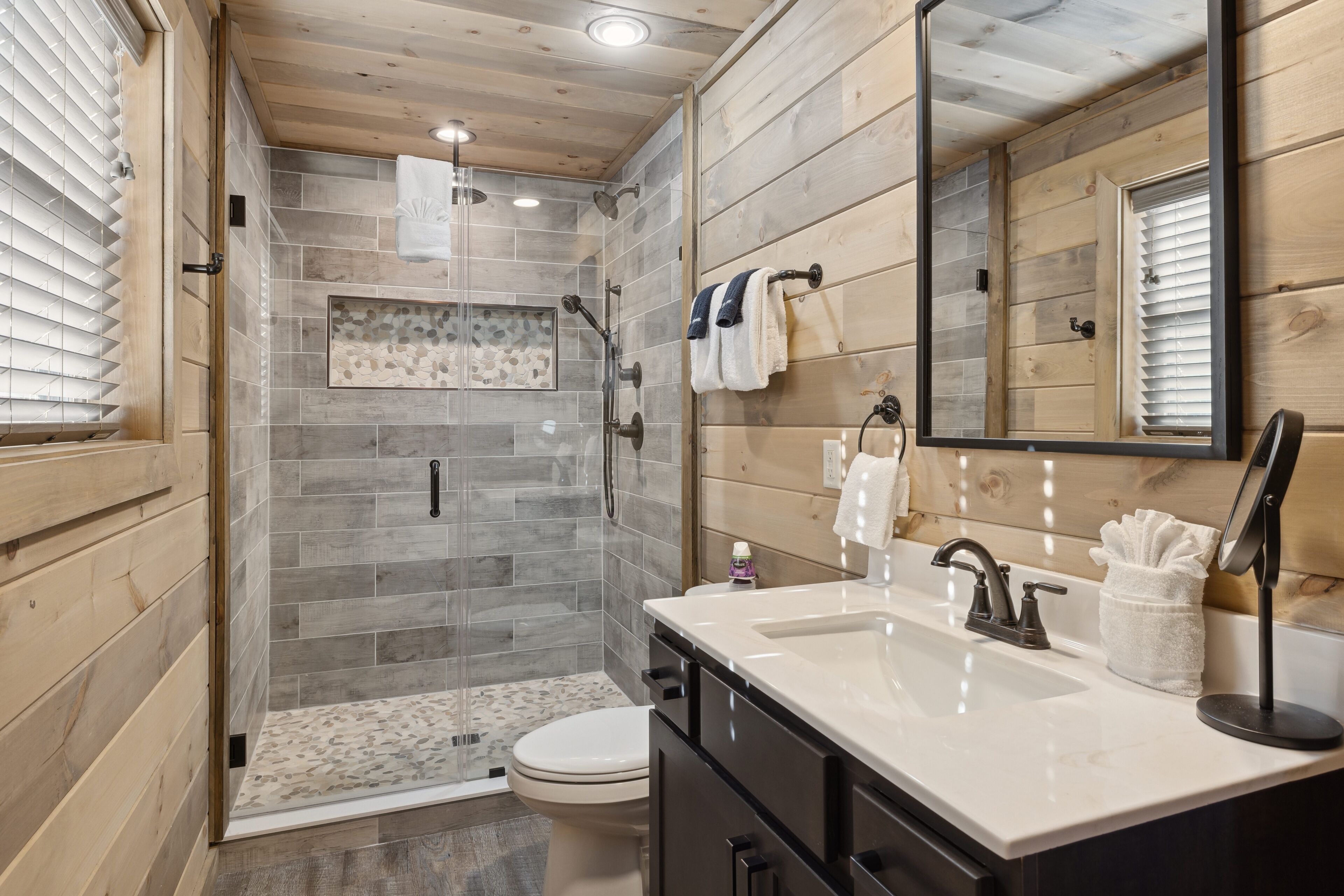 Un baño moderno con cabina de ducha de vidrio, un lavabo blanco y un mueble de tocador de madera.