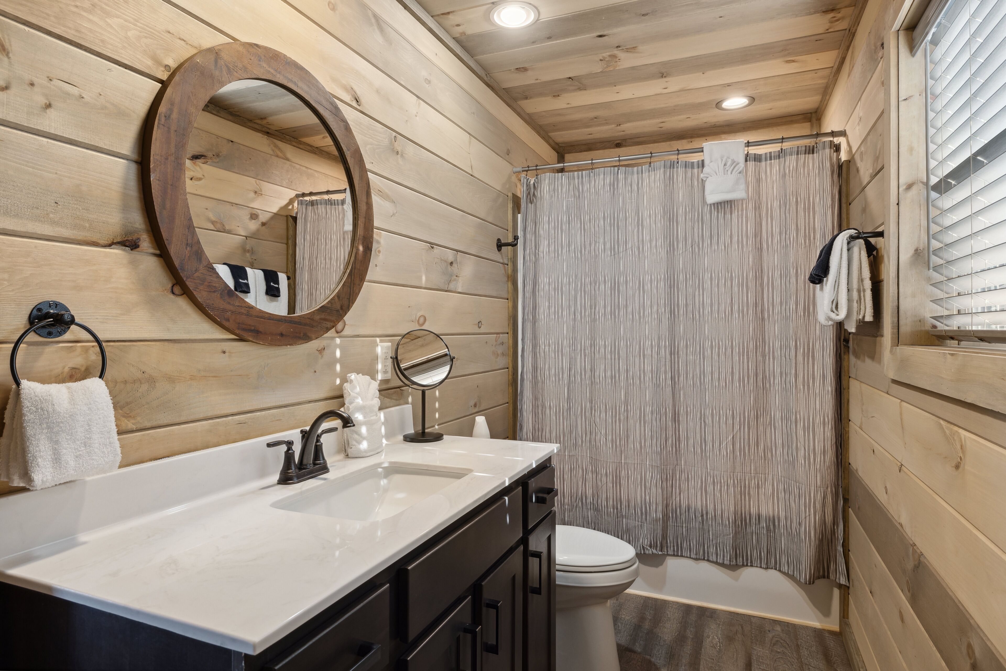 A wooden cabin bathroom with a white sink, black cabinets, a round mirror, and a shower curtain.