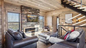 A cozy living room with a stone fireplace, leather sofas, and a wooden staircase. - Treehouse Lodge 5 Bedroom Cabin by RedAwning (Sevierville)