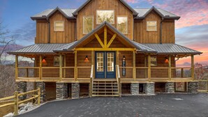 A large wooden lodge with a prominent front entrance, multiple windows, and a balcony. - Treehouse Lodge 5 Bedroom Cabin by RedAwning (Sevierville)