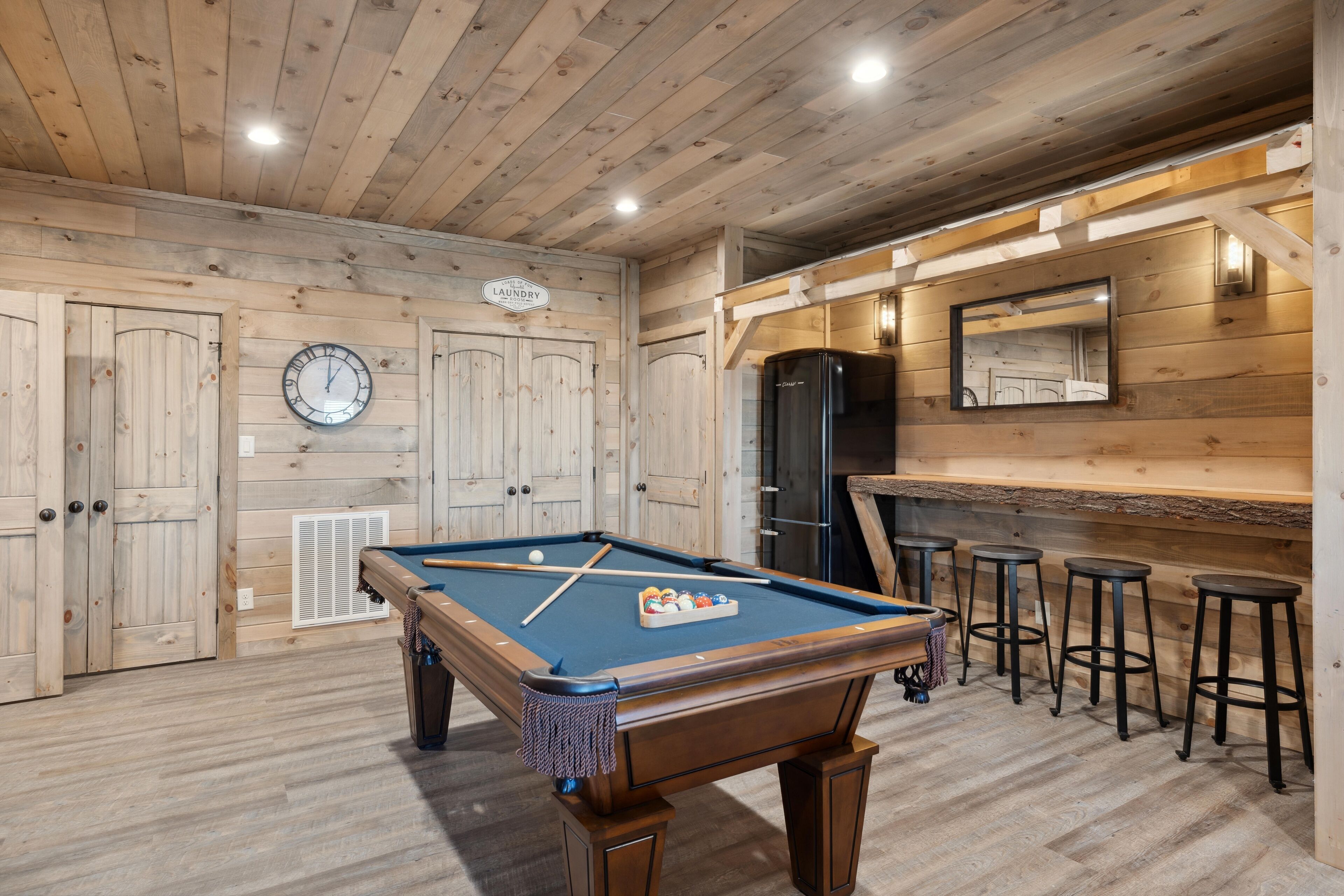 A pool table with a clock and a bar area with stools.