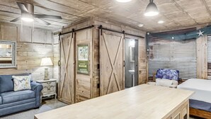 A room with a wooden ceiling, a blue sofa, a wooden table, and a bed with a blue and white bedspread. - Casas Coastal Experience Cabin B 1 Bedroom Cottage by RedAwning (Rockport)