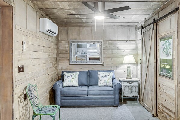Una habitación acogedora con un sofá azul, un sillón verde, una mesita con una lámpara y un espejo enmarcado en la pared.