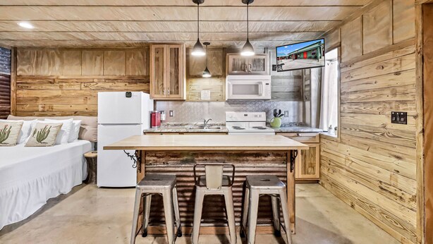 A compact kitchen with wooden walls, a central island with stools, a refrigerator, a microwave, and a sink.