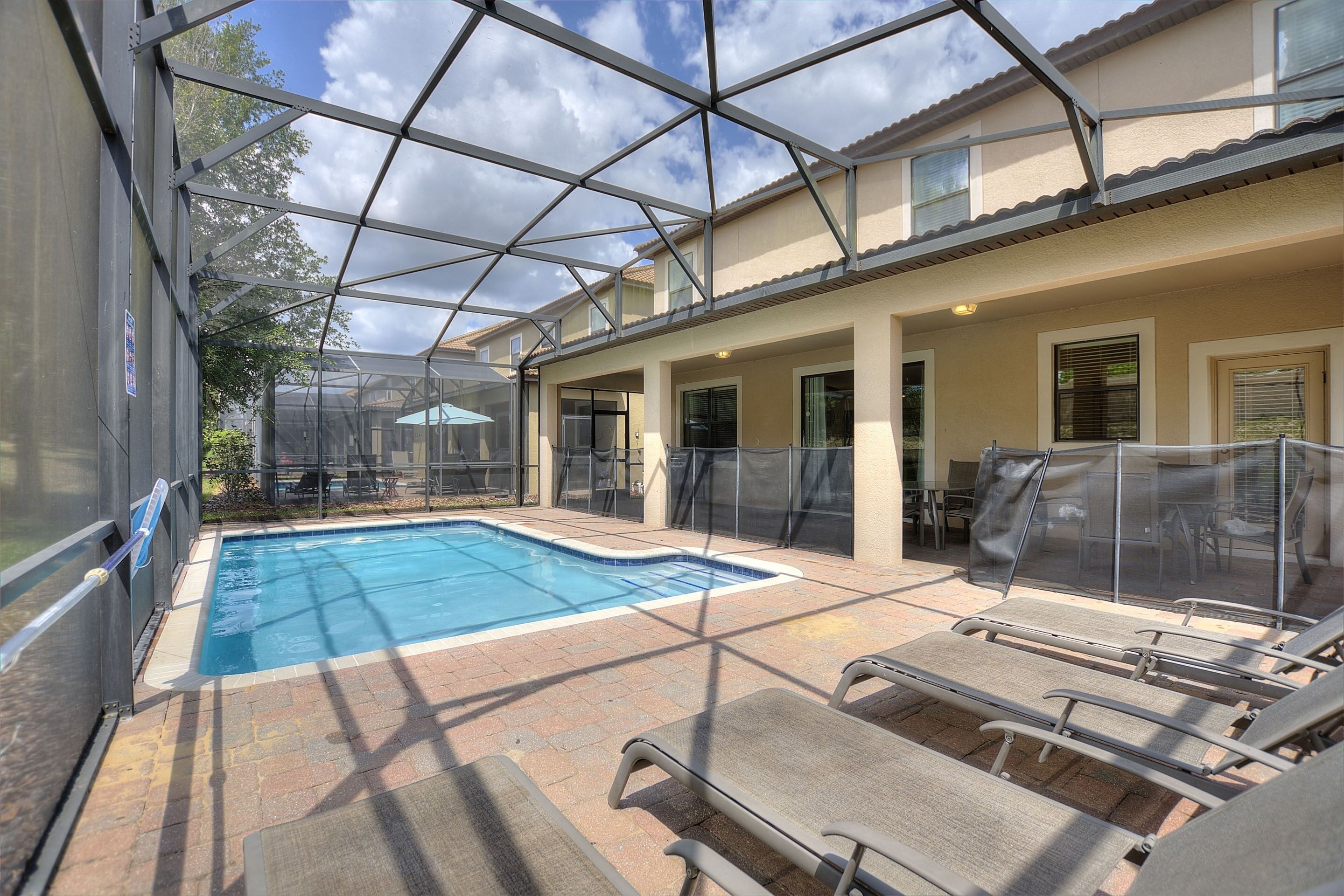 A pool area with a glass enclosure, lounge chairs, and a patio with a tiled floor.